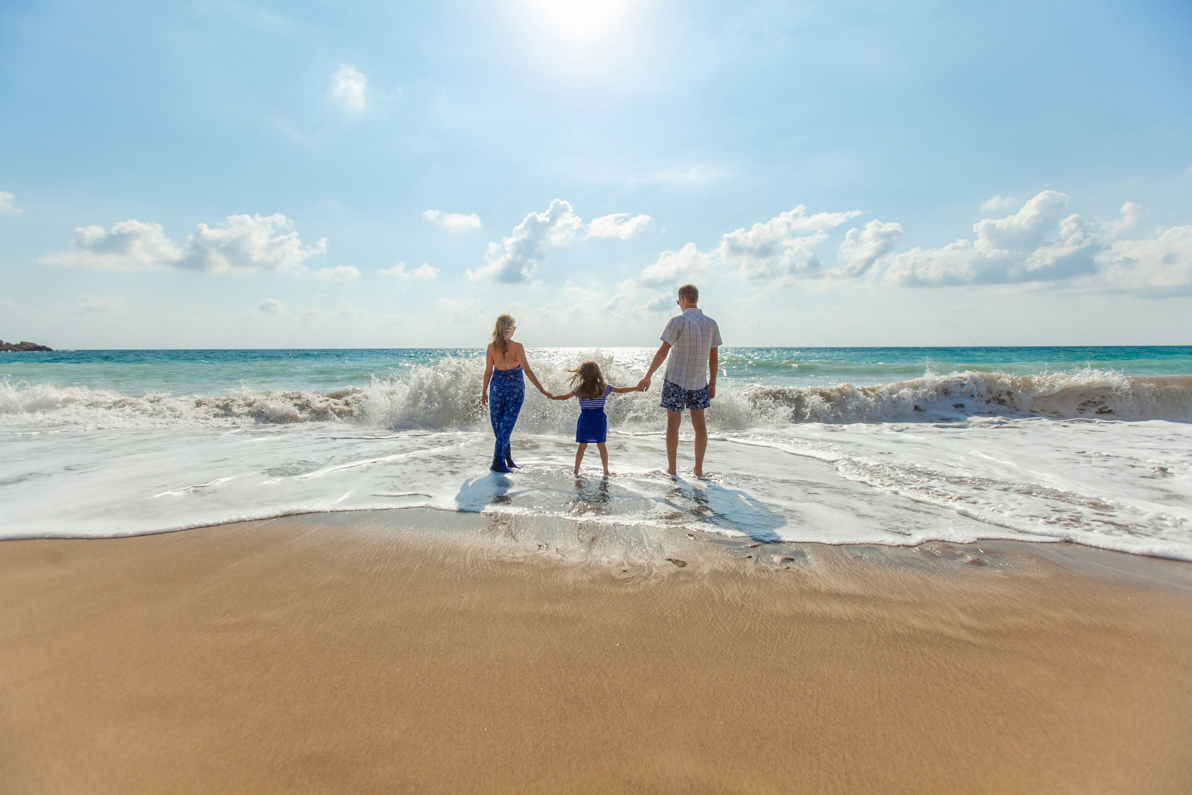 A family of three walking into the surf on a beach