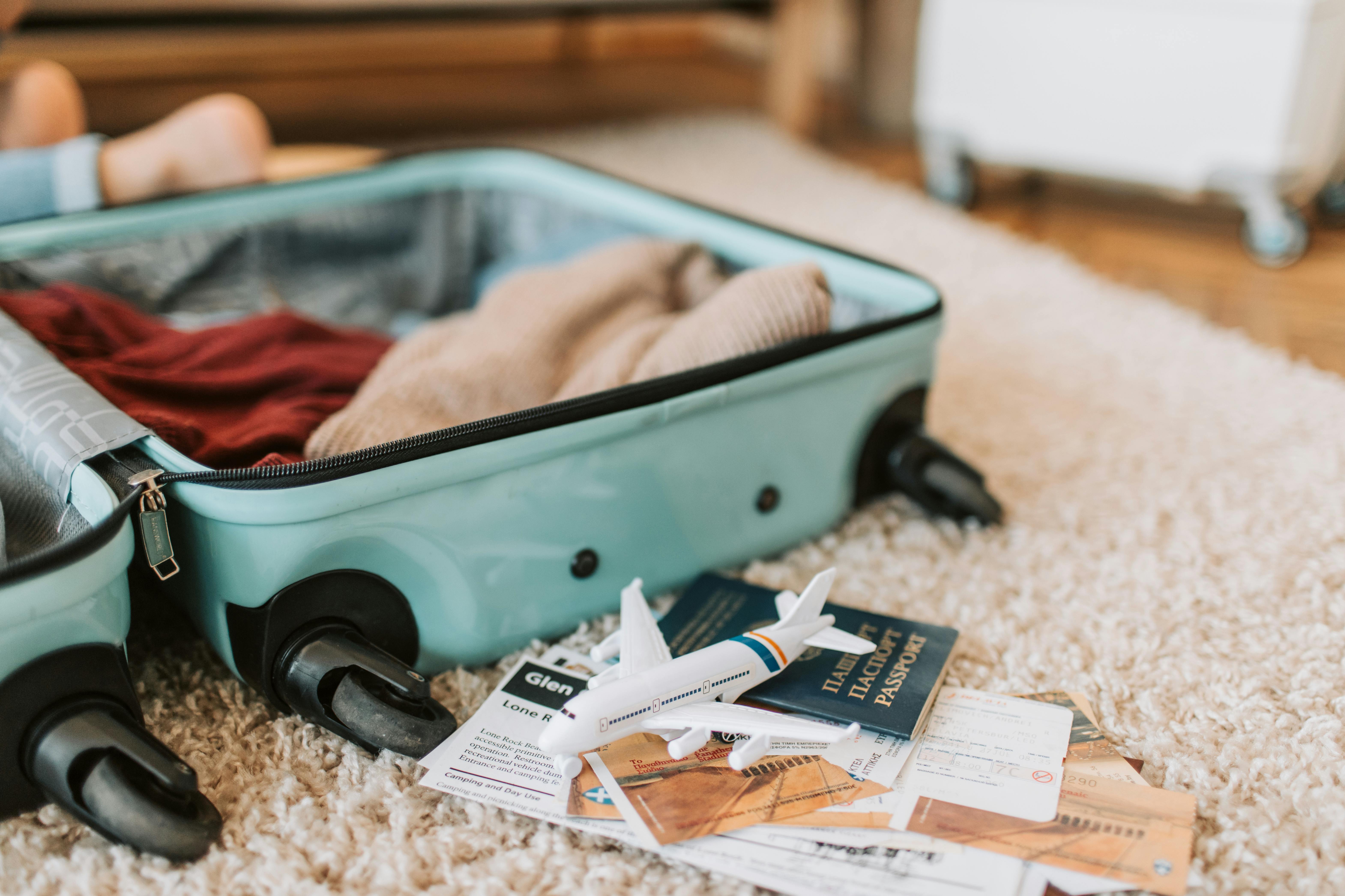 An open turquoise suitcase with clothes and travel documents on a rug