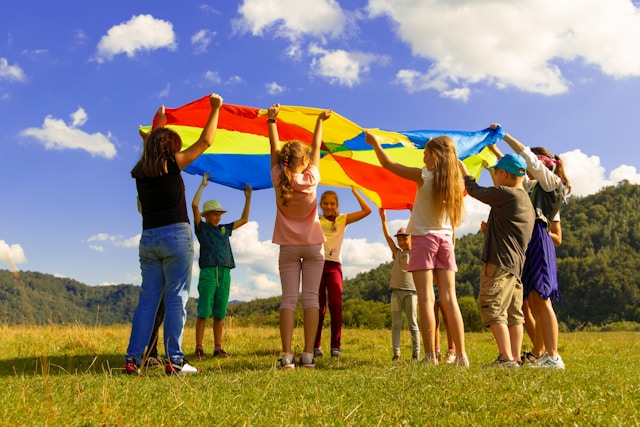 Children and adults holding a rainbow parachute on a sunny field