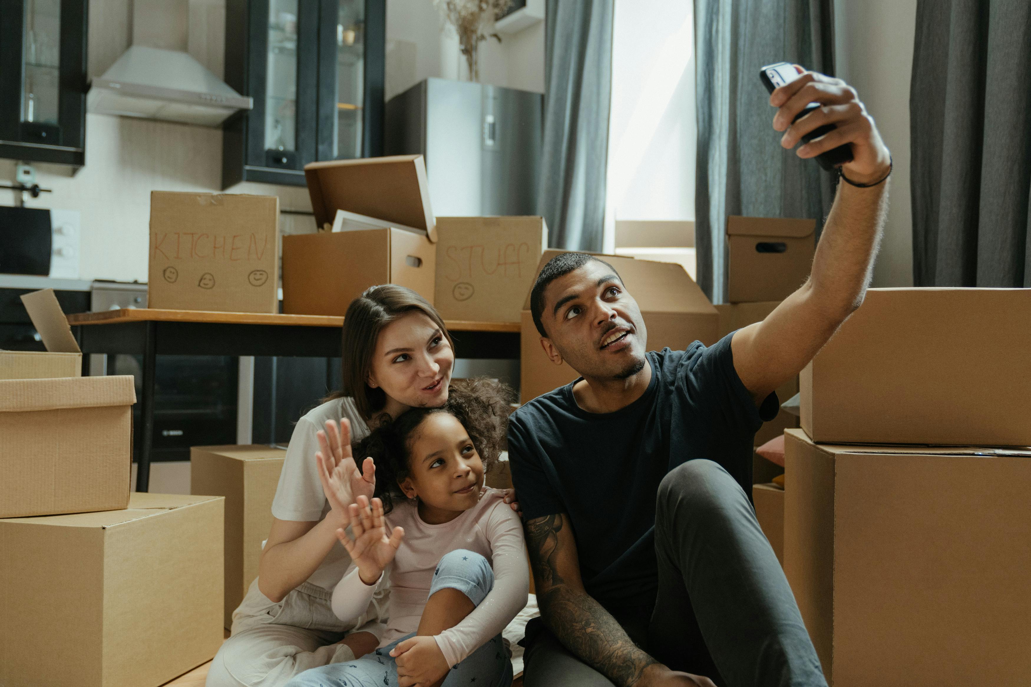 A couple and a child sitting among moving boxes and taking a selfie